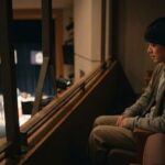 劇場の見切れ席に座り、ステージを見つめる日本人の観客。視界が遮られる様子。