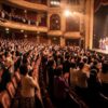 人気ミュージカル公演の終演後、満員の劇場でスタンディングオベーションを送る日本人観客の様子。チケット争奪戦を勝ち抜いた喜びと興奮を表現。