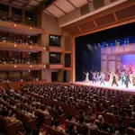 煌びやかな照明に照らされた、満員の観客で埋め尽くされた大劇場のステージ。豪華な衣装を纏った俳優たちが躍動するミュージカルの公演風景。劇場の熱気と感動が伝わる一枚。