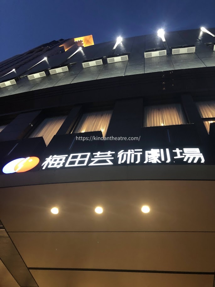 ライトアップされたロゴ看板が暗闇に浮かび上がる夜の梅田芸術劇場外観